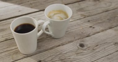 Video of white cup of coffee with milk and cup of black coffee over wooden background. Coffee, refreshment and beverages.