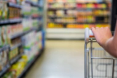 Cropped image of person with shopping cart on aisle at supermarket