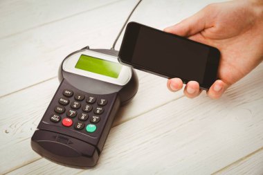 Close-up of cropped hand holding mobile phone with credit card reader on table
