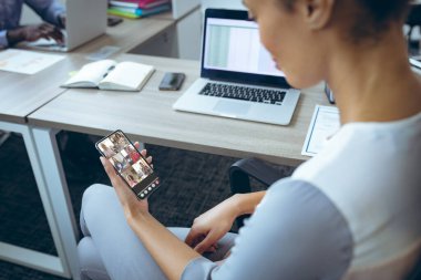 Çift ırklı iş kadını iş arkadaşlarıyla iş yerinde akıllı telefonlardan konferans videosu. değiştirilmemiş, kablosuz teknoloji, tartışma, internet, iş dünyası, takım çalışması.