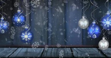 Animation of snow falling over christmas baubles on blue background. Christmas tradition and celebration concept digitally generated video.