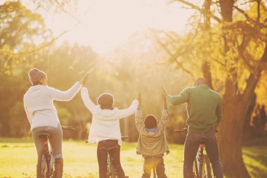 Rear view of family doing high five while sitting on bicycles at park
