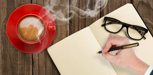 Overhead view of hot tea by hand writing on book against wooden table