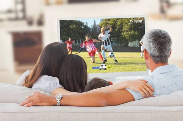 Football player kicking ball against family watching television together on sofa