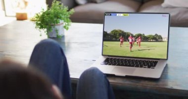 Kanepede oturan ve dizüstü bilgisayarda futbol izleyen bir kadının videosu. Spor, rekabet ve ailece evde vakit geçirmek..