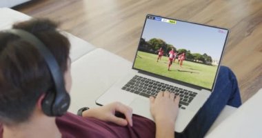Kafkasyalı bir adamın kanepede oturup dizüstü bilgisayarda futbol izlediği bir video. Spor, rekabet ve ailece evde vakit geçirmek..