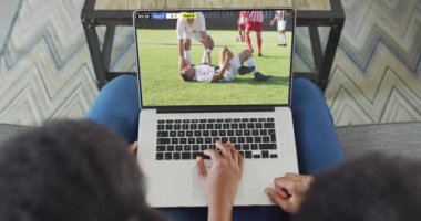 Afro-Amerikan çiftin kanepede oturup dizüstü bilgisayardan futbol izlediği bir video. Spor, rekabet ve ailece evde vakit geçirmek..