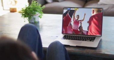 Kanepede oturan ve dizüstü bilgisayarda futbol izleyen bir kadının videosu. Spor, rekabet ve ailece evde vakit geçirmek..