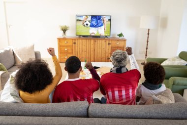 Mutlu Afro-Amerikan ailesi birlikte futbol maçı izleyip kanepede oturuyor. Futbol, rekabet, tezahürat ve birlikte zaman geçirme..