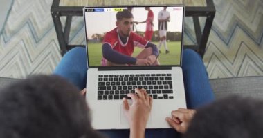 Afro-Amerikan çiftin kanepede oturup dizüstü bilgisayardan futbol izlediği bir video. Spor, rekabet ve ailece evde vakit geçirmek..