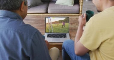 Kanepede oturup dizüstü bilgisayarda futbol izleyen çeşitli erkek arkadaşların videosu. Spor, rekabet ve ailece evde vakit geçirmek..