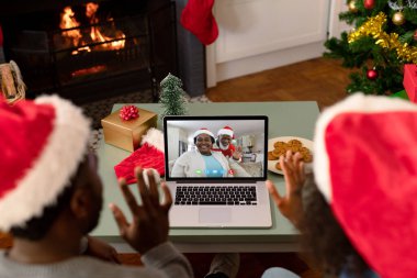 El sallayan çift, gülümseyen Afro-Amerikan bir çiftle dizüstü bilgisayarlı Noel videosu görüşmesi yapıyor. Noel, şenlik ve iletişim teknolojisi.