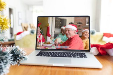 Noel Baba şapkalı, dizüstü bilgisayarlı, çeşitli kıdemli arkadaşlar arayüz ekranında gülümsüyor. Noel, şenlik ve iletişim teknolojisi.