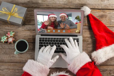 Noel Baba dizüstü bilgisayarla Kafkasyalı baba ve kızına el sallarken görüntülü arama yapıyor. Noel, şenlik ve iletişim teknolojisi.