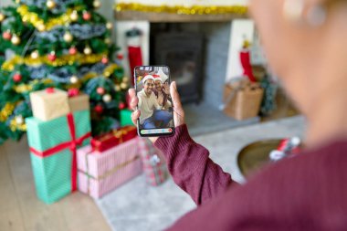 Noel Baba ve yetişkin oğlu Noel Baba şapkalı mutlu bir baba ile akıllı telefon görüşmesi yapan bir kadın. Noel, şenlik ve iletişim teknolojisi.