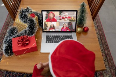Noel Baba şapkalı beyaz bir kadın arkadaşlarıyla yılbaşı dizüstü bilgisayarında görüntülü görüşme yapıyor. Noel, şenlik ve iletişim teknolojisi.
