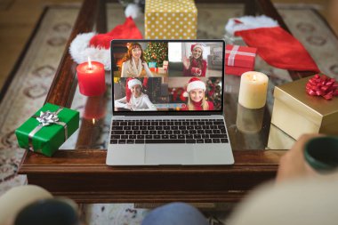 Laptop grubunda Noel Baba şapkası takmış gülümseyen beyaz kadın arkadaşlar Noel 'de ekran diyoruz. Noel, şenlik ve iletişim teknolojisi.