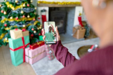 Yaşlı, Afro-Amerikan bir adamla Noel 'de akıllı telefon görüşmesi yapan bir kadın. Noel, şenlik ve iletişim teknolojisi.