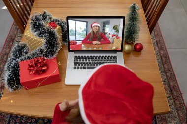 Noel Baba şapkalı beyaz kadın, kız arkadaşıyla birlikte dizüstü bilgisayarda görüntülü görüşme yapıyor. Noel, şenlik ve iletişim teknolojisi.
