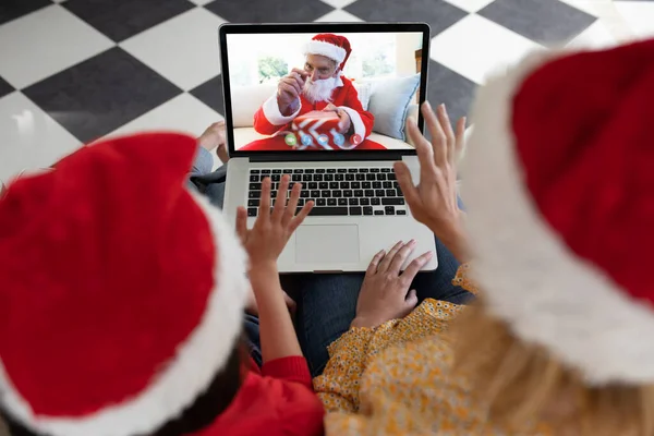 サンタの服を着た先輩とラップトップのクリスマスビデオ通話をする母親と娘を振っています クリスマスやお祭りや通信技術は — ストック写真
