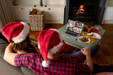 Noel Baba şapkalı beyaz bir çift arkadaşlarıyla yılbaşı laptopunda video görüşmesi yapıyor. Noel, şenlik ve iletişim teknolojisi.