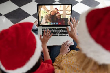 Noel bilgisayarında arkadaşlarıyla Noel Baba şapkası takan beyaz bir anne ve kız. Noel, şenlik ve iletişim teknolojisi.