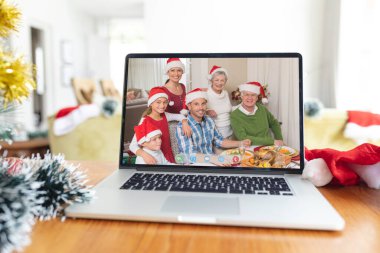 Bilgisayarlı Noel Baba şapkalı, çok nesildir gülümseyen beyaz bir aile. Noel, şenlik ve iletişim teknolojisi.