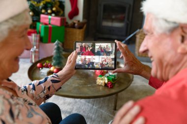 Noel Baba şapkalı beyaz çift, arkadaşları ve ailesiyle birlikte tabletten yılbaşı görüntülerini arıyor. Noel, şenlik ve iletişim teknolojisi.
