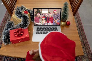 Kafkasyalı bir kadın, üç nesildir gülümseyen beyaz bir aileyle dizüstü bilgisayarla yılbaşı videosu çekiyor. Noel, şenlik ve iletişim teknolojisi.
