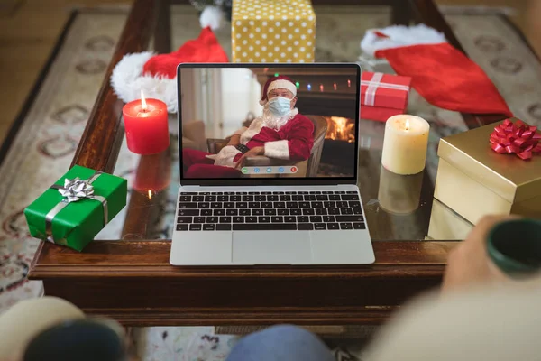 stock image Santa claus wearing face mask on laptop video call screen at christmas time. christmas, festivity and communication technology during covid 19 pandemic.