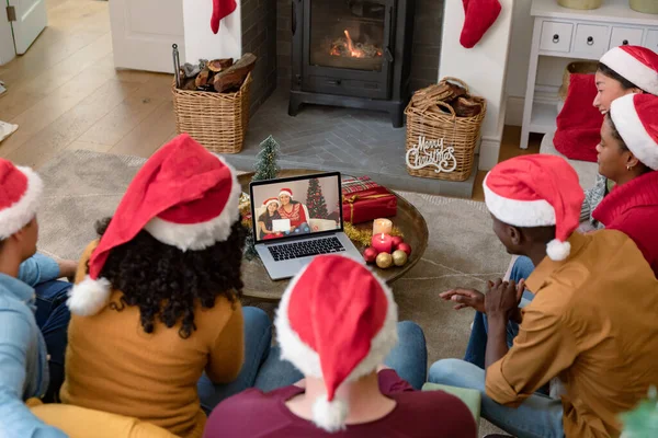 Group of diverse friends in santa hats on christmas video call on laptop with friends. christmas, festivity and communication technology.