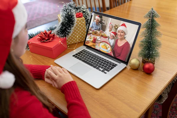 サンタの帽子の白人女性は ディナーテーブルで笑顔の家族とクリスマスのラップトップビデオ通話を作ります クリスマスやお祭りや通信技術は — ストック写真