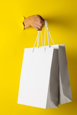 Sarı arka planda el ele alışveriş torbalarının kompozisyonu. Perakende, alışveriş ve Kara Cuma konsepti.