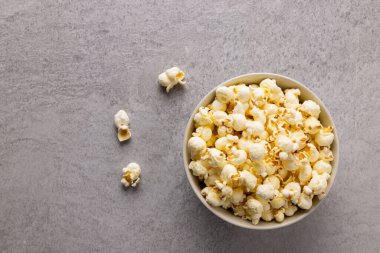 Gri yüzeyde kasede patlamış mısır resmi. Yiyecek, atıştırmalık, sinema ve Amerikan mutfağı konsepti.