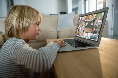 Beyaz çocuk ekranda çeşitli ilköğretim öğrencileri gülümserken görüntülü konuşma için laptop kullanıyor. iletişim teknolojisi ve çevrimiçi eğitim, dijital kompozit resim.