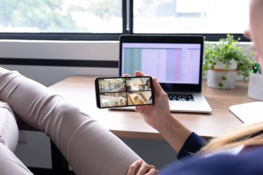 Beyaz kadın ofisteki güvenlik kameralarından evi gören akıllı telefonu kullanıyor. güvenlik, güvenlik, izleme ve dijital arayüz.