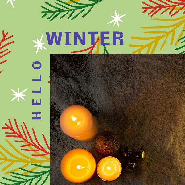 Composition of hello winter text over candles and fir trees. Winter and celebration concept digitally generated image.