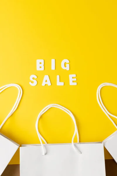 Composition of paper bags and big sale text on yellow background. Retail, shopping and black friday concept.