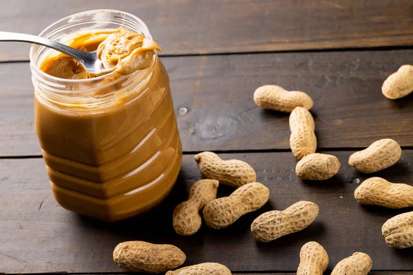 Image of jar with peanut butter and nuts on wooden surface. Food, breakfast, nutrition and american cuisine concept.