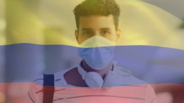 Kolombiya bayrağının şehir caddesinde yüz maskesi takan Latin adamın üzerinde dalgalanması. covid 19 salgın konsepti boyunca dijital olarak üretilen küresel sağlık önlemleri.