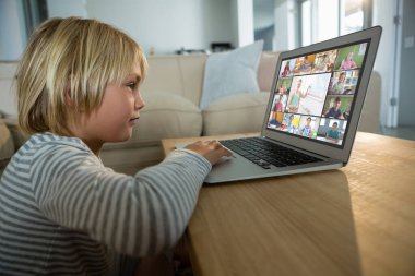 Beyaz çocuk ekranda çeşitli ilköğretim öğrencileri gülümserken görüntülü konuşma için laptop kullanıyor. iletişim teknolojisi ve çevrimiçi eğitim, dijital kompozit resim.