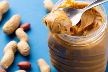 Mavi yüzeyde fıstık ezmeli kaşık ve kavanoz resmi. Yiyecek, kahvaltı, beslenme ve Amerikan mutfağı konsepti.