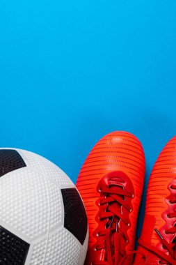 Futbol ve kırmızı ayakkabıların kompozisyonu mavi arka planda fotokopi alanı ile. Spor, hareket, eğitim ve aktif yaşam tarzı kavramı.