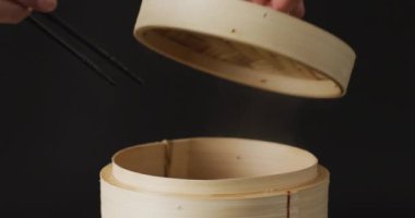 Siyah arka planda bambu buharı içinde gyoza hamur tatlısı olan çubuklarla el ele tutuşmak. Yiyecek, içecek ve renk konsepti.
