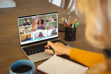 Beyaz bir kadın ekranda çeşitli ilkokul öğrencilerinin gülümsediği bir video görüşmesi için dizüstü bilgisayar kullanıyor. iletişim teknolojisi ve çevrimiçi eğitim, dijital kompozit resim.