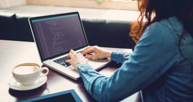 Masada oturan ve ekranda kodlama olan dizüstü bilgisayar kullanan beyaz kadın programcının orta bölümü. Kodlama, programlama ve bilgisayar teknolojisi dijital kompozit görüntü.