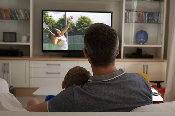Rear view of father and son sitting at home together watching tennis match on tv. sports, competition, entertainment and technology concept digital composite image.