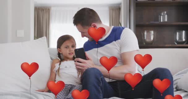 利用沙发上的智能手机在高加索父亲和女儿的上空制作心形气球动画 爱情和通信技术概念数码视频 — 图库视频影像