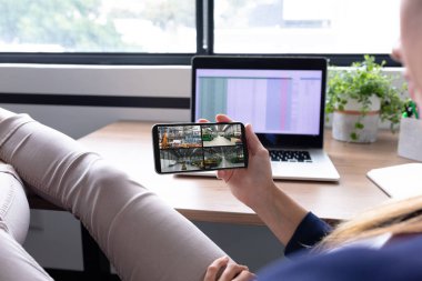 Beyaz bir kadın akıllı telefon tutuyor ve ekranda deponun güvenlik kameralarını görüyor. güvenlik, güvenlik, izleme ve dijital arayüz.