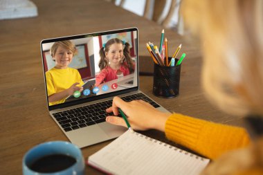 Beyaz bir kadın ekranda çeşitli ilkokul öğrencilerinin gülümsediği bir video görüşmesi için dizüstü bilgisayar kullanıyor. iletişim teknolojisi ve çevrimiçi eğitim, dijital kompozit resim.